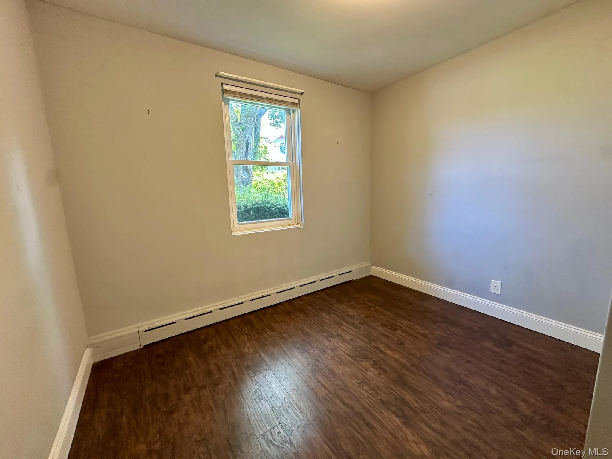 Empty room with dark wood-style flooring and baseboard heating Empty room with dark wood-style flooring and baseboard heating