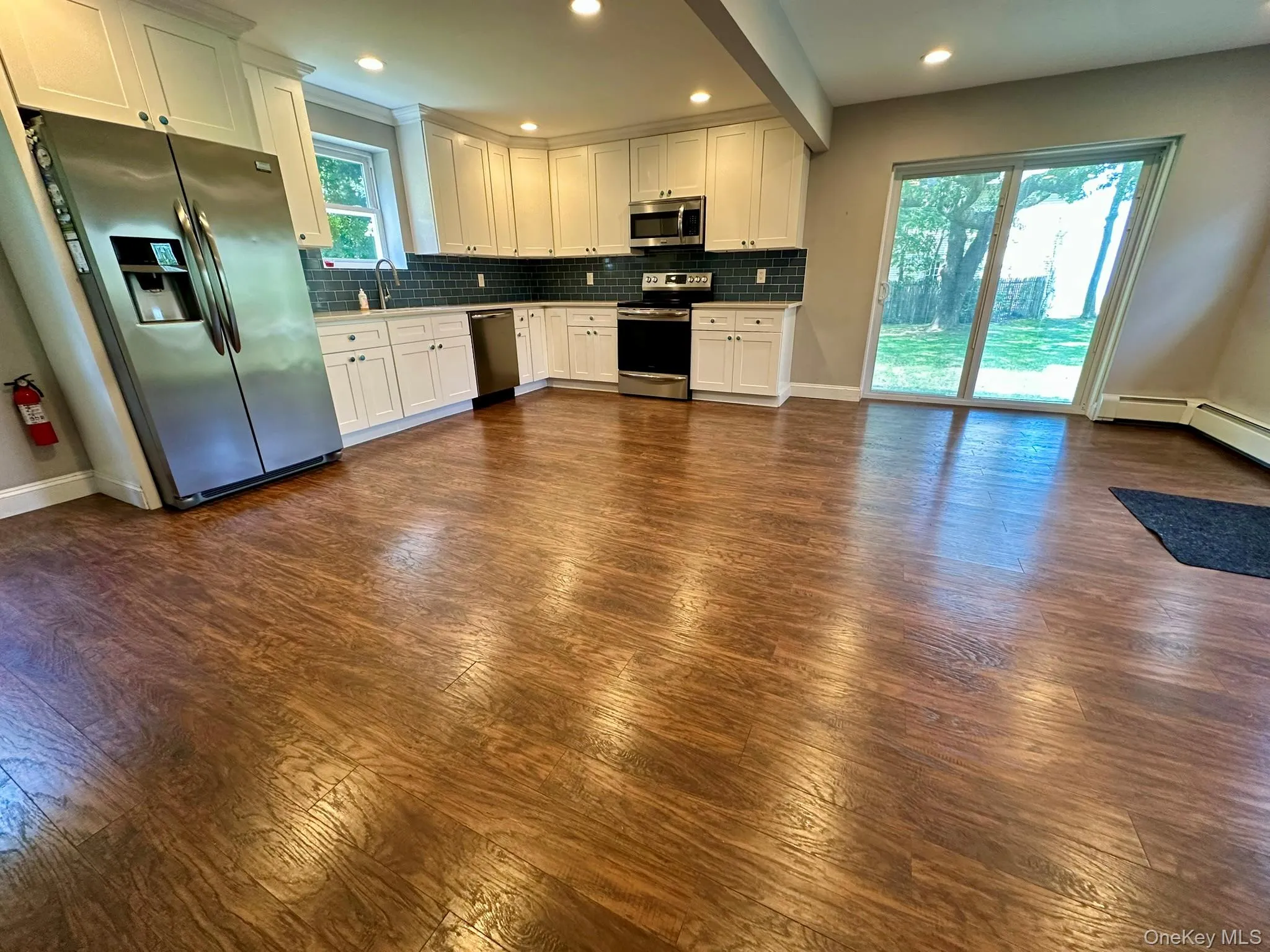 Kitchen with white cabinets, stainless steel appliances, tasteful backsplash, dark wood-type flooring, and recessed lighting Kitchen with white cabinets, stainless steel appliances, tasteful backsplash, dark wood-type flooring, and recessed lighting