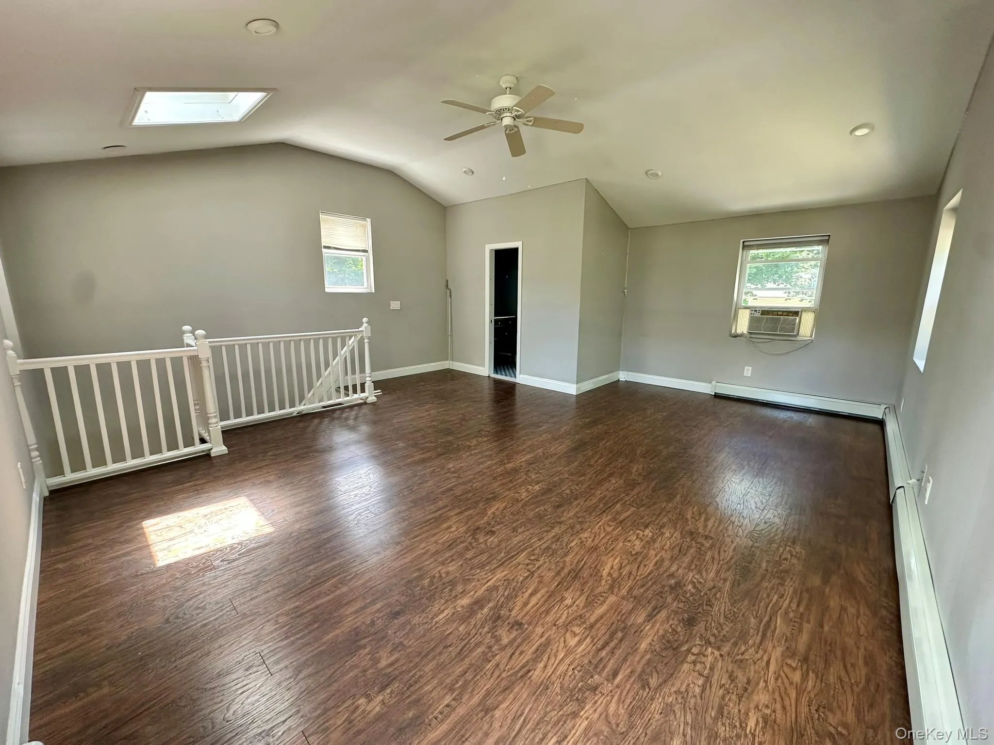 Empty room with a skylight, dark wood-type flooring, lofted ceiling, a baseboard heating unit, and a ceiling fan Empty room with a skylight, dark wood-type flooring, lofted ceiling, a baseboard heating unit, and a ceiling fan