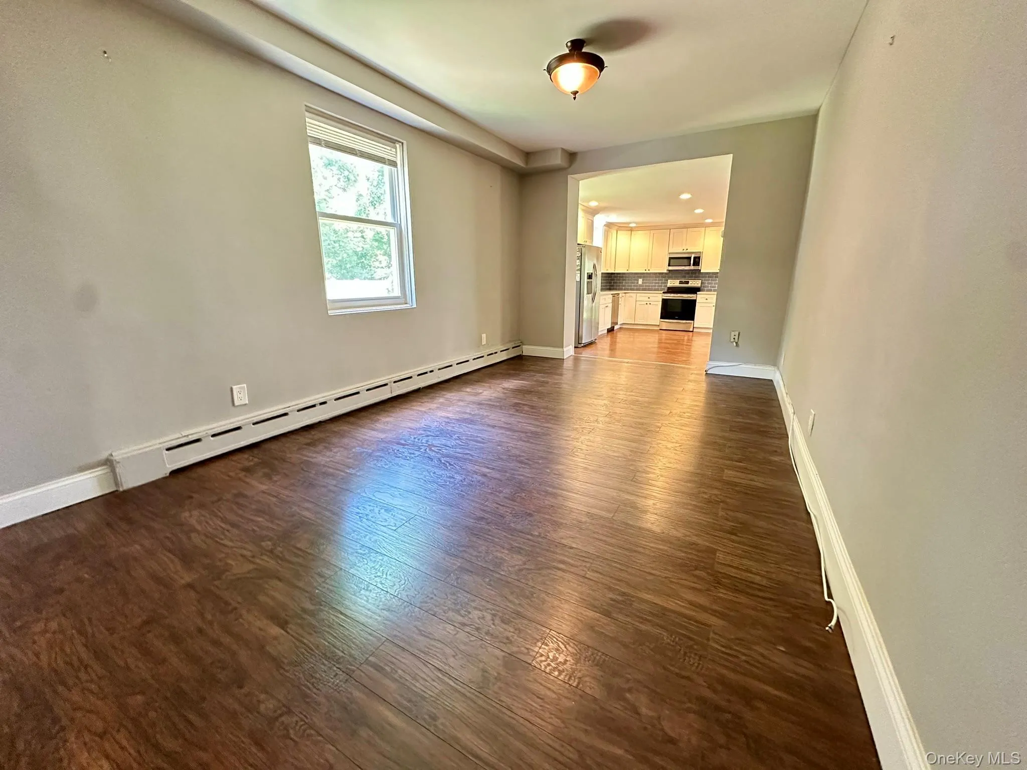 Unfurnished living room featuring dark wood finished floors and a baseboard heating unit Unfurnished living room featuring dark wood finished floors and a baseboard heating unit
