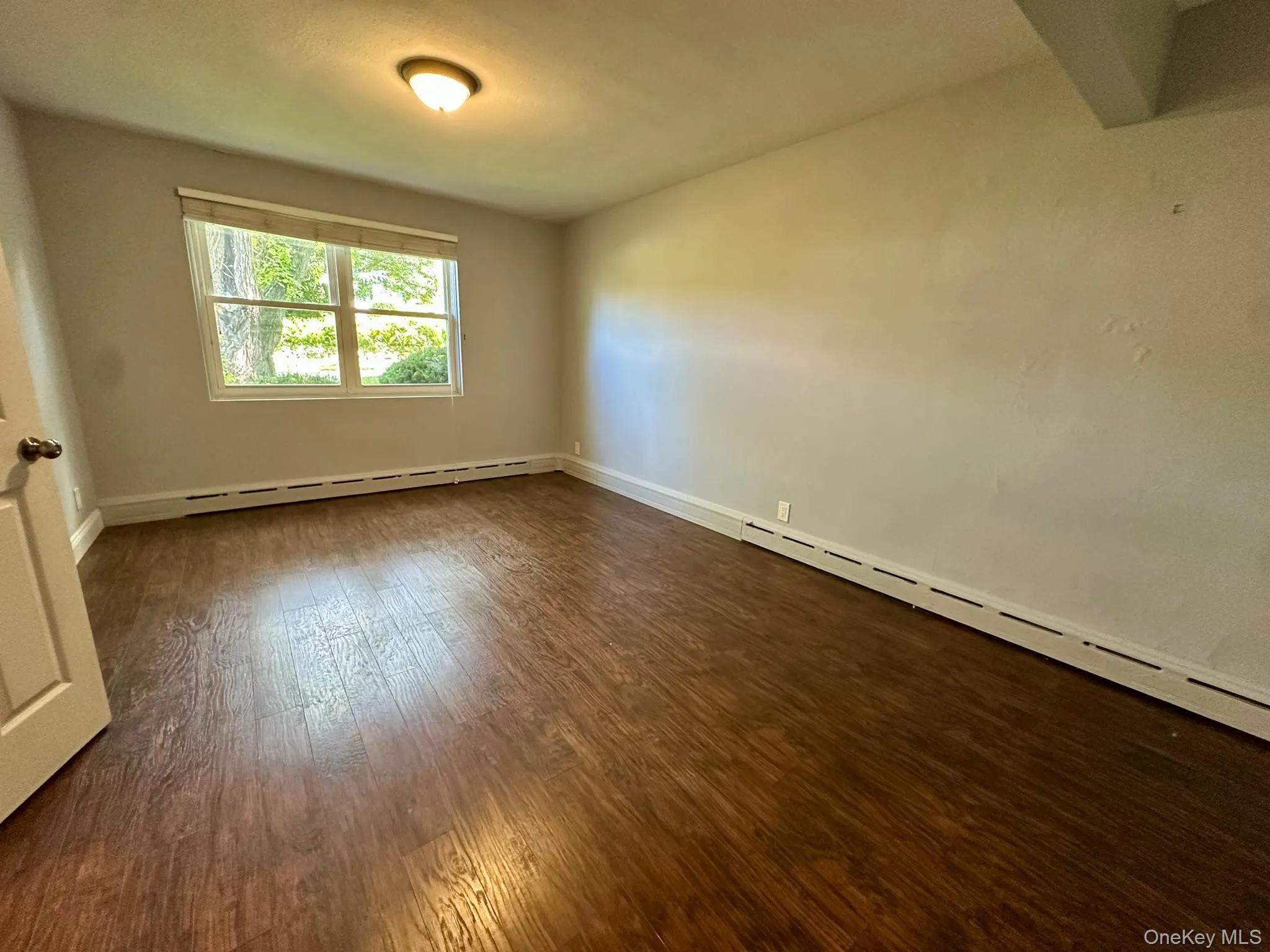 Spare room featuring dark wood-style flooring and a baseboard radiator Spare room featuring dark wood-style flooring and a baseboard radiator