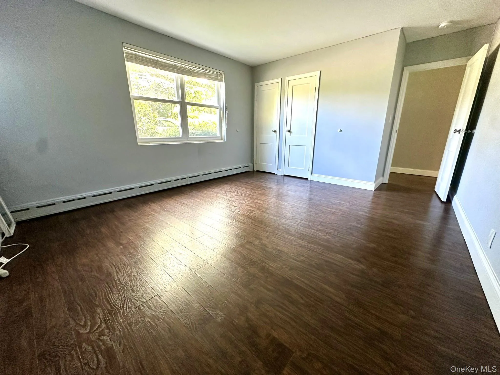 Unfurnished bedroom with baseboard heating and dark wood-style floors Unfurnished bedroom with baseboard heating and dark wood-style floors