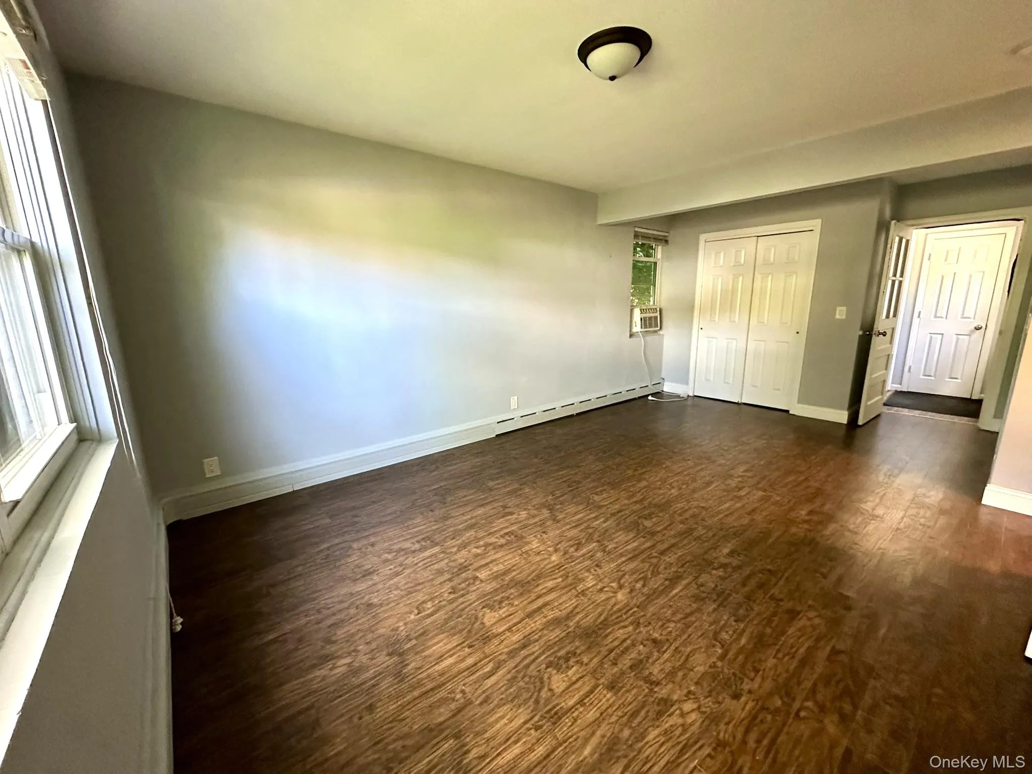 Unfurnished bedroom featuring dark wood-style floors, a closet, and a baseboard radiator Unfurnished bedroom featuring dark wood-style floors, a closet, and a baseboard radiator