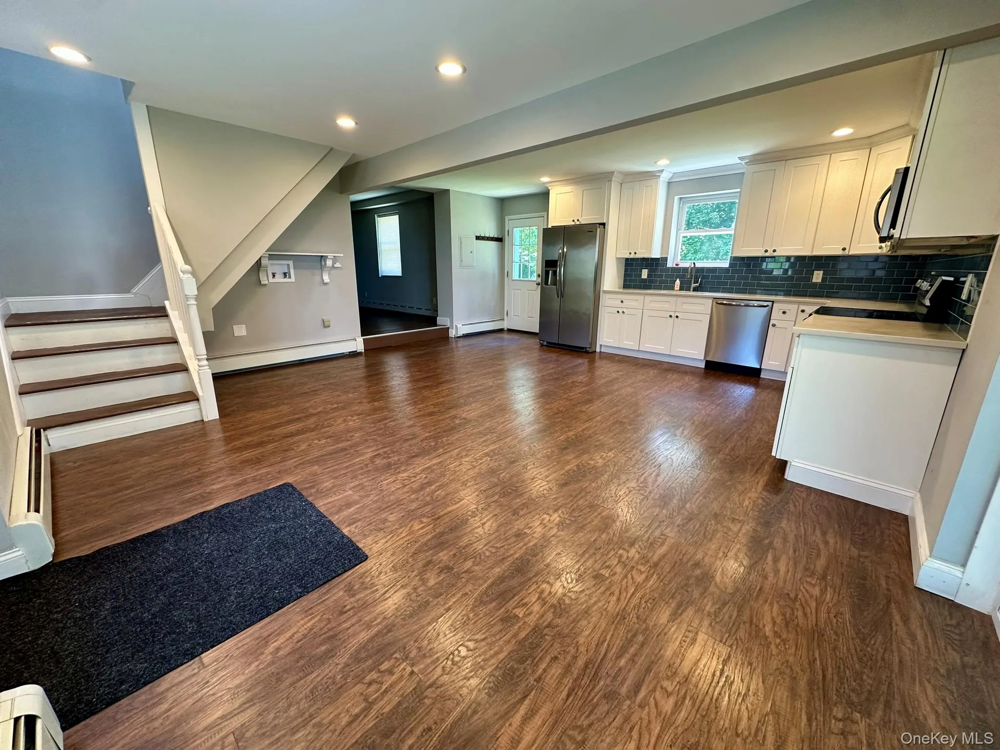 Kitchen with decorative backsplash, white cabinetry, dark wood-style flooring, recessed lighting, and appliances with stainless steel finishes Kitchen with decorative backsplash, white cabinetry, dark wood-style flooring, recessed lighting, and appliances with stainless steel finishes