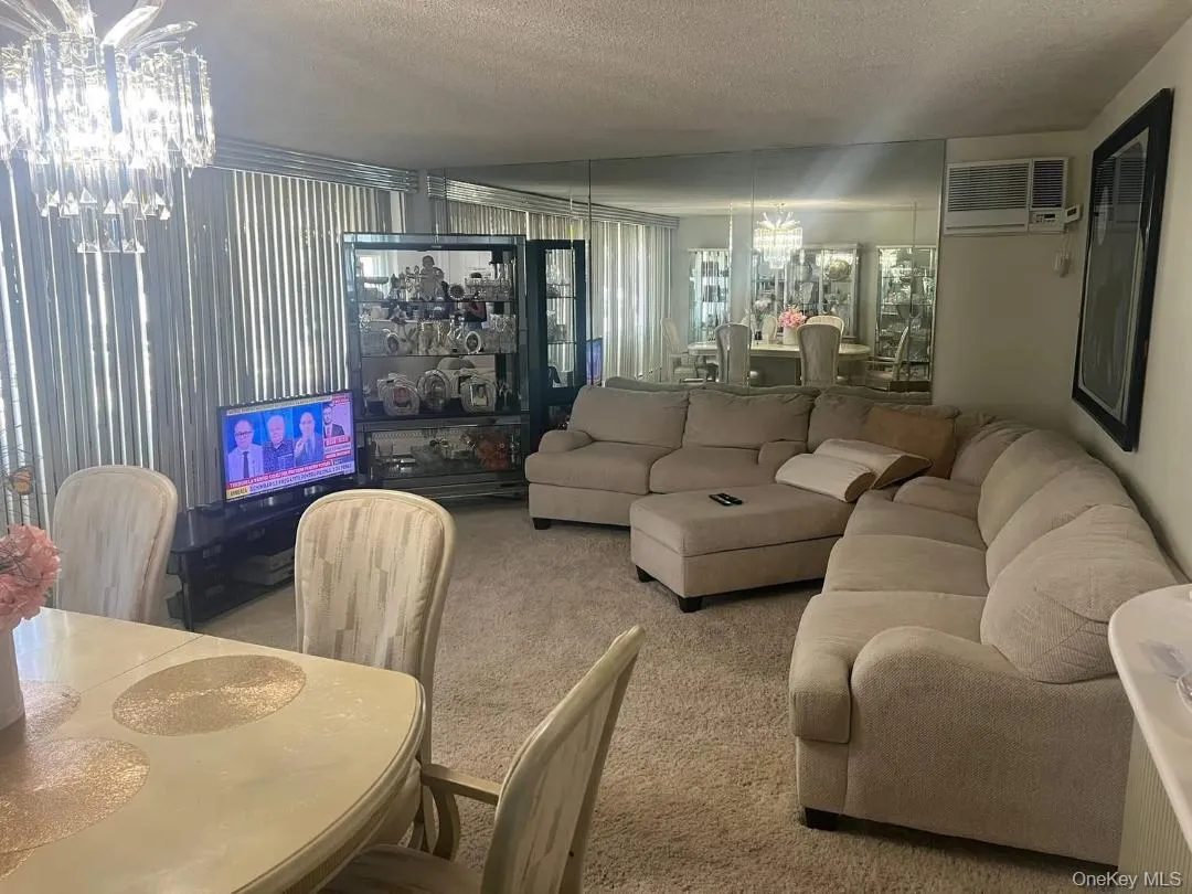 Carpeted living room featuring a chandelier, a textured ceiling, and a wall mounted air conditioner Carpeted living room featuring a chandelier, a textured ceiling, and a wall mounted air conditioner