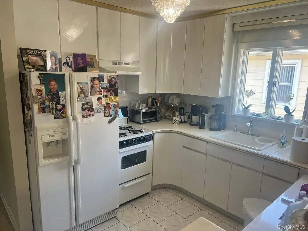 Kitchen featuring white appliances, light countertops, under cabinet range hood, a textured ceiling, and white cabinets Kitchen featuring white appliances, light countertops, under cabinet range hood, a textured ceiling, and white cabinets