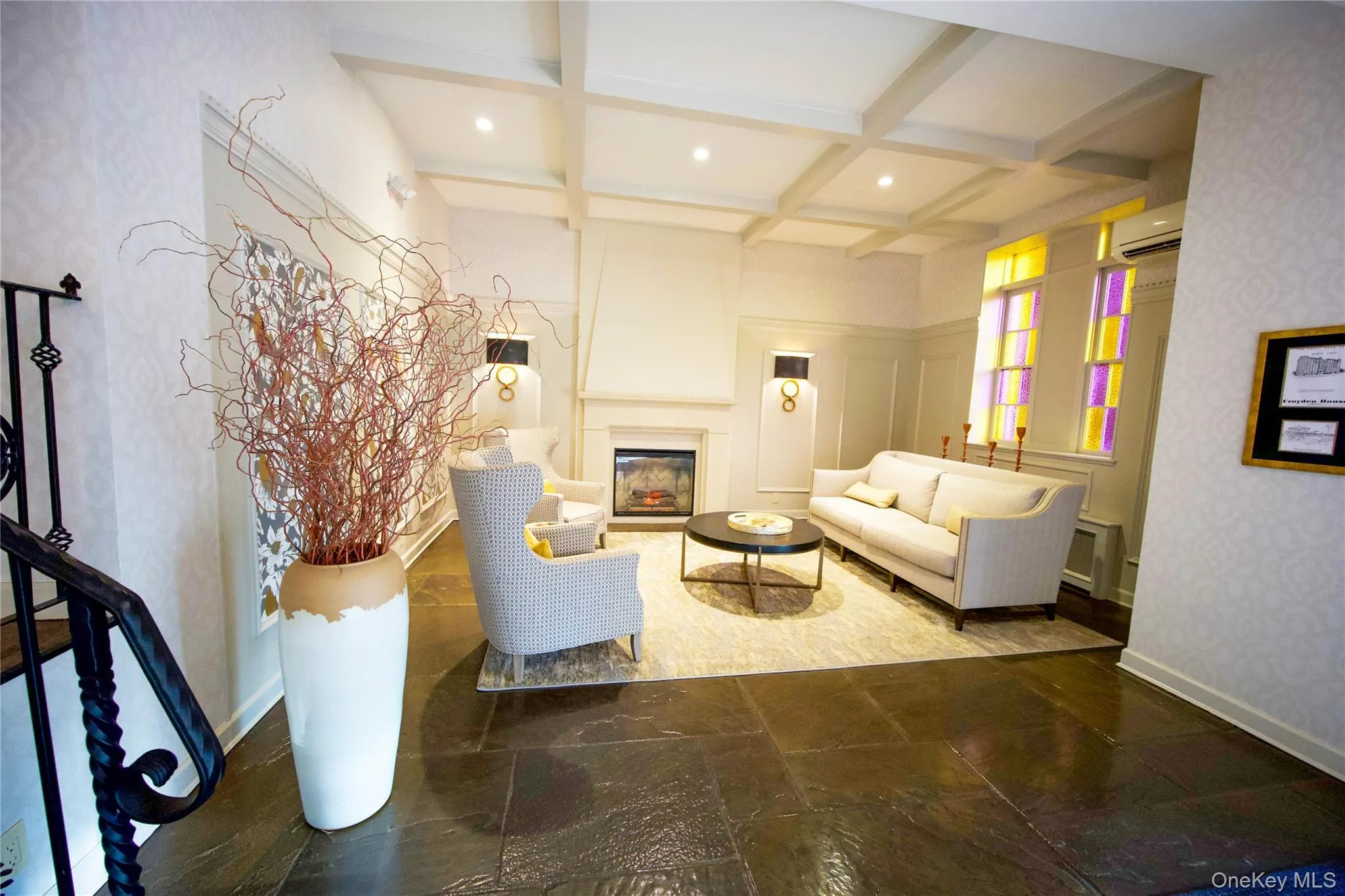 Living room featuring coffered ceiling, beamed ceiling, a large fireplace, wallpapered walls, and a wall mounted air conditioner Living room featuring coffered ceiling, beamed ceiling, a large fireplace, wallpapered walls, and a wall mounted air conditioner