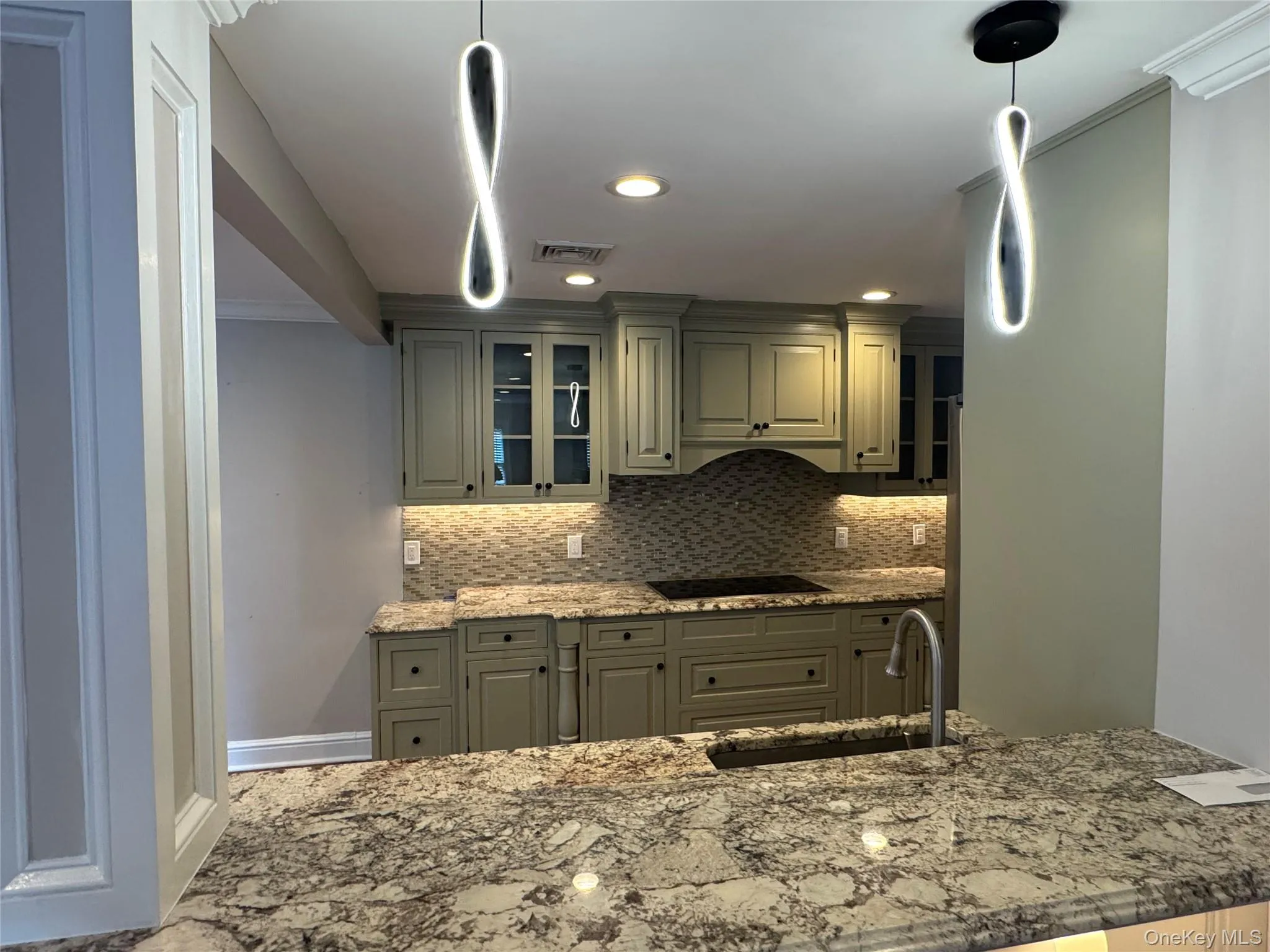 Kitchen featuring backsplash, glass insert cabinets, light stone countertops, gray cabinets, and recessed lighting Kitchen featuring backsplash, glass insert cabinets, light stone countertops, gray cabinets, and recessed lighting