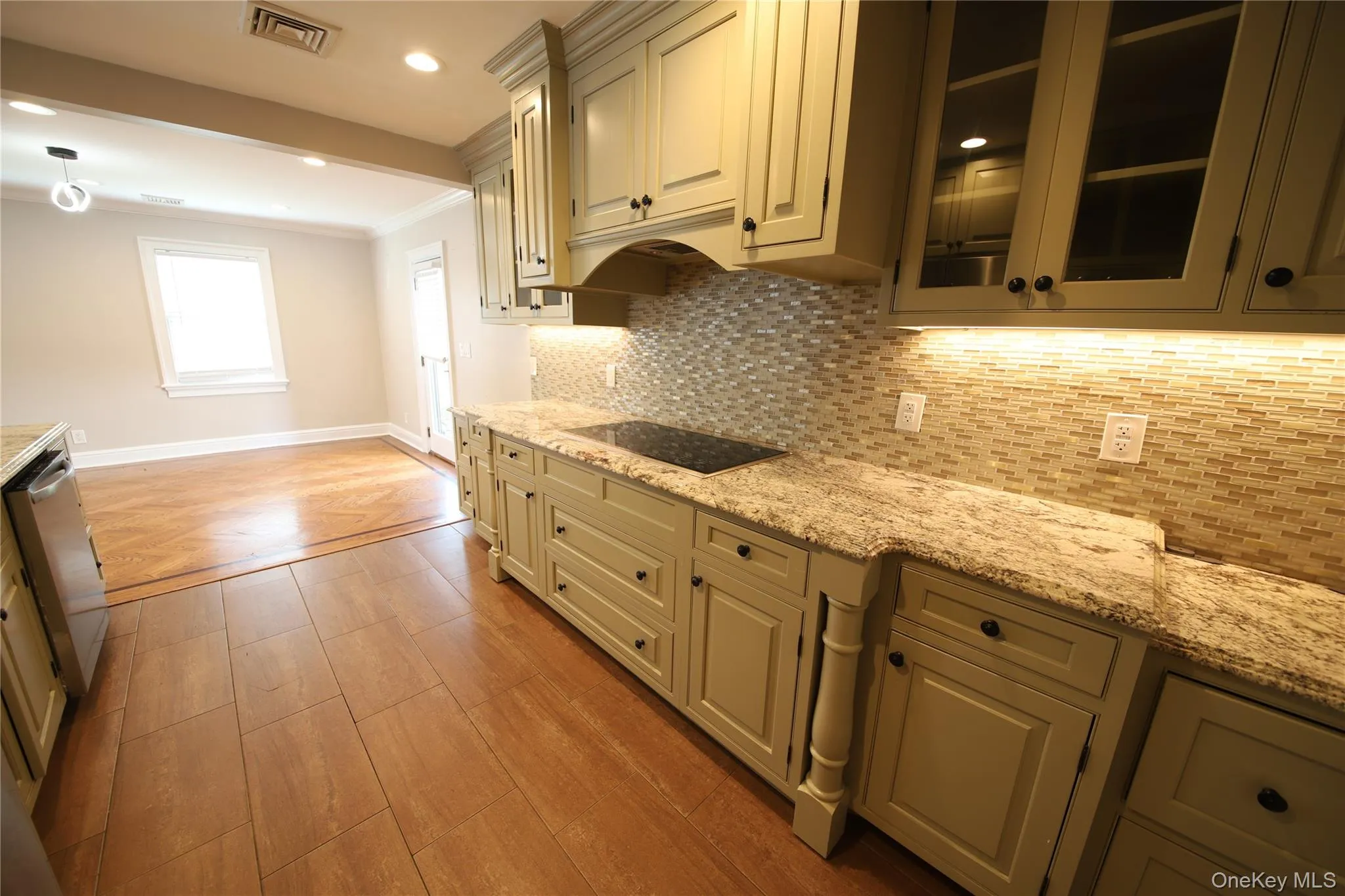 Kitchen with backsplash, ornamental molding, glass insert cabinets, light stone counters, and light wood-style flooring Kitchen with backsplash, ornamental molding, glass insert cabinets, light stone counters, and light wood-style flooring