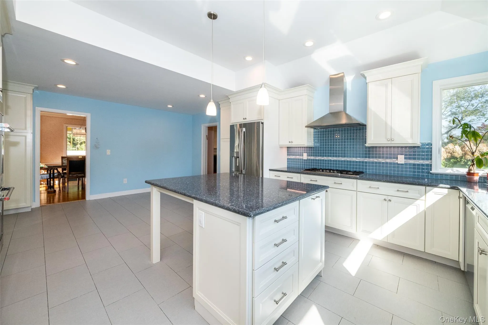 Kitchen featuring a kitchen bar, wall chimney range hood, a center island, decorative backsplash, and light tile patterned floors Kitchen featuring a kitchen bar, wall chimney range hood, a center island, decorative backsplash, and light tile patterned floors