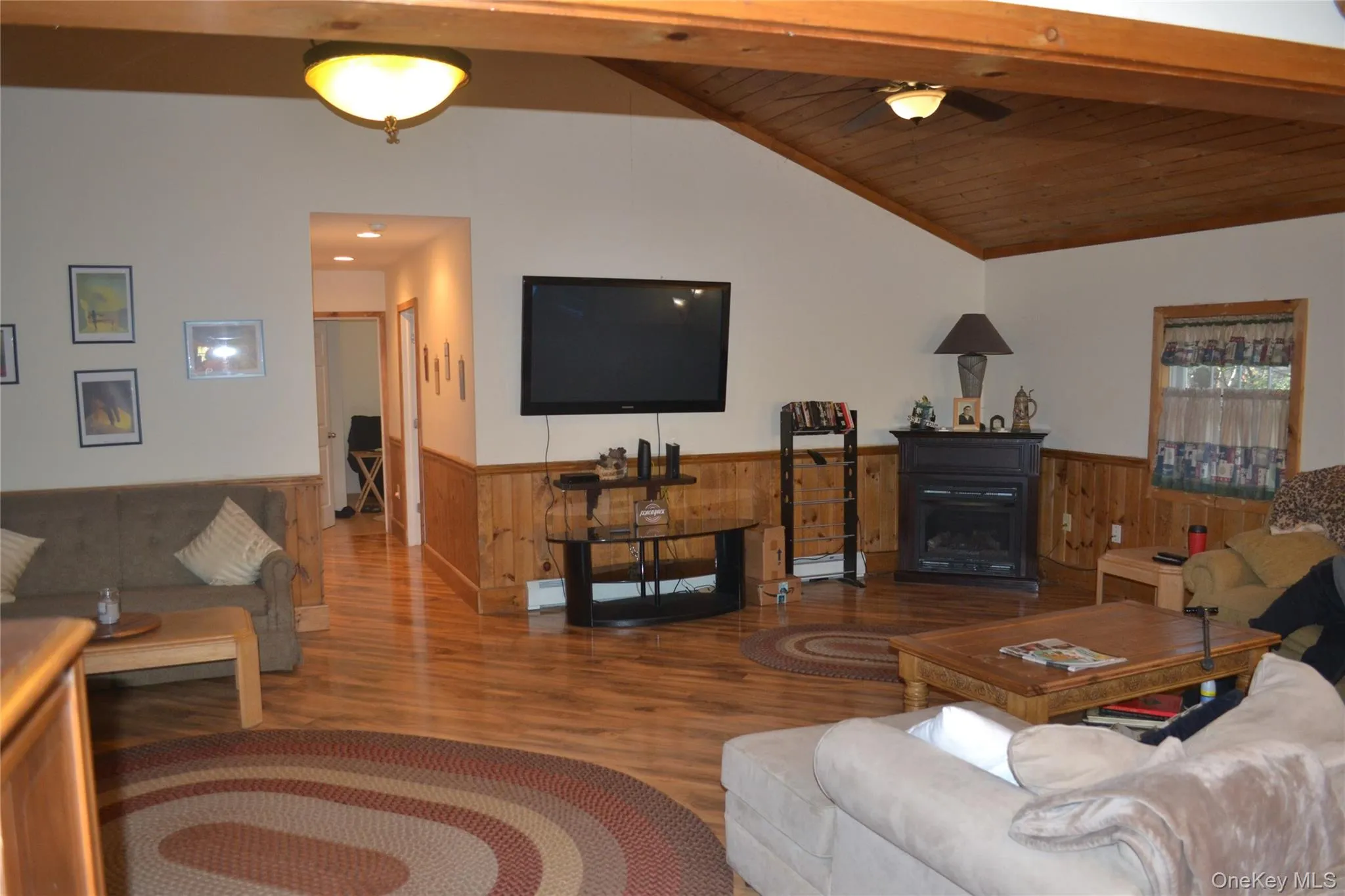 Living area featuring wood finished floors, wooden walls, a wainscoted wall, wood ceiling, and a ceiling fan Living area featuring wood finished floors, wooden walls, a wainscoted wall, wood ceiling, and a ceiling fan
