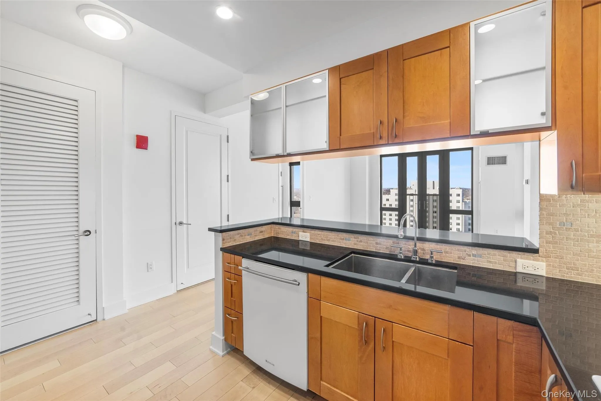 Kitchen with brown cabinetry, white dishwasher, light wood finished floors, decorative backsplash, and recessed lighting Kitchen with brown cabinetry, white dishwasher, light wood finished floors, decorative backsplash, and recessed lighting