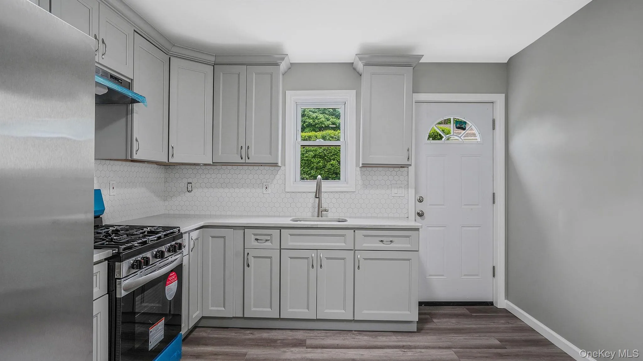 Kitchen featuring stainless steel appliances, backsplash, dark wood-style floors, and under cabinet range hood Kitchen featuring stainless steel appliances, backsplash, dark wood-style floors, and under cabinet range hood