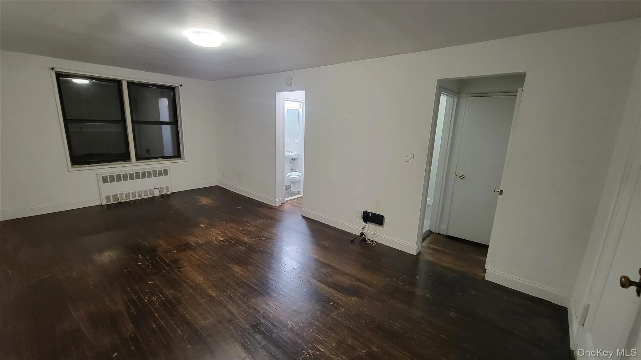 Unfurnished room featuring dark wood finished floors and radiator heating unit Unfurnished room featuring dark wood finished floors and radiator heating unit