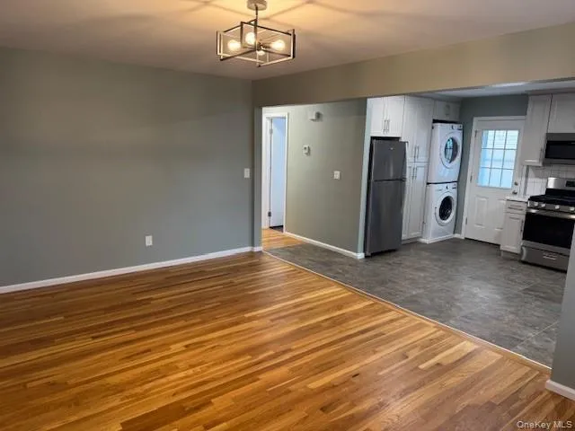 Kitchen featuring appliances with stainless steel finishes, white cabinetry, dark wood-style flooring, stacked washer / dryer, and a chandelier Kitchen featuring appliances with stainless steel finishes, white cabinetry, dark wood-style flooring, stacked washer / dryer, and a chandelier