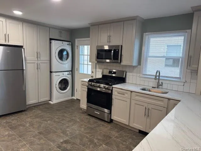 Kitchen featuring appliances with stainless steel finishes, stacked washer / drying machine, tasteful backsplash, and light stone counters Kitchen featuring appliances with stainless steel finishes, stacked washer / drying machine, tasteful backsplash, and light stone counters