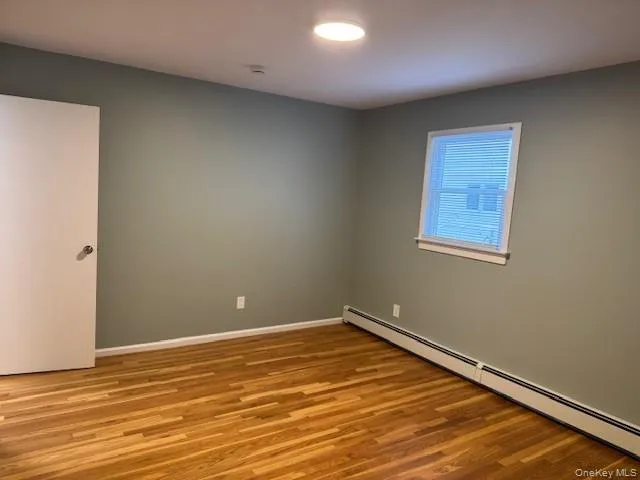 Unfurnished room featuring a baseboard heating unit and wood finished floors Unfurnished room featuring a baseboard heating unit and wood finished floors