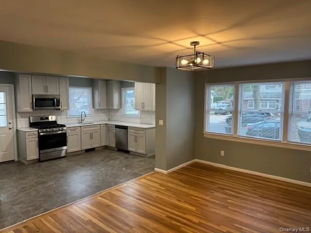 Kitchen featuring decorative backsplash, stainless steel appliances, light countertops, dark wood-type flooring, and a chandelier Kitchen featuring decorative backsplash, stainless steel appliances, light countertops, dark wood-type flooring, and a chandelier