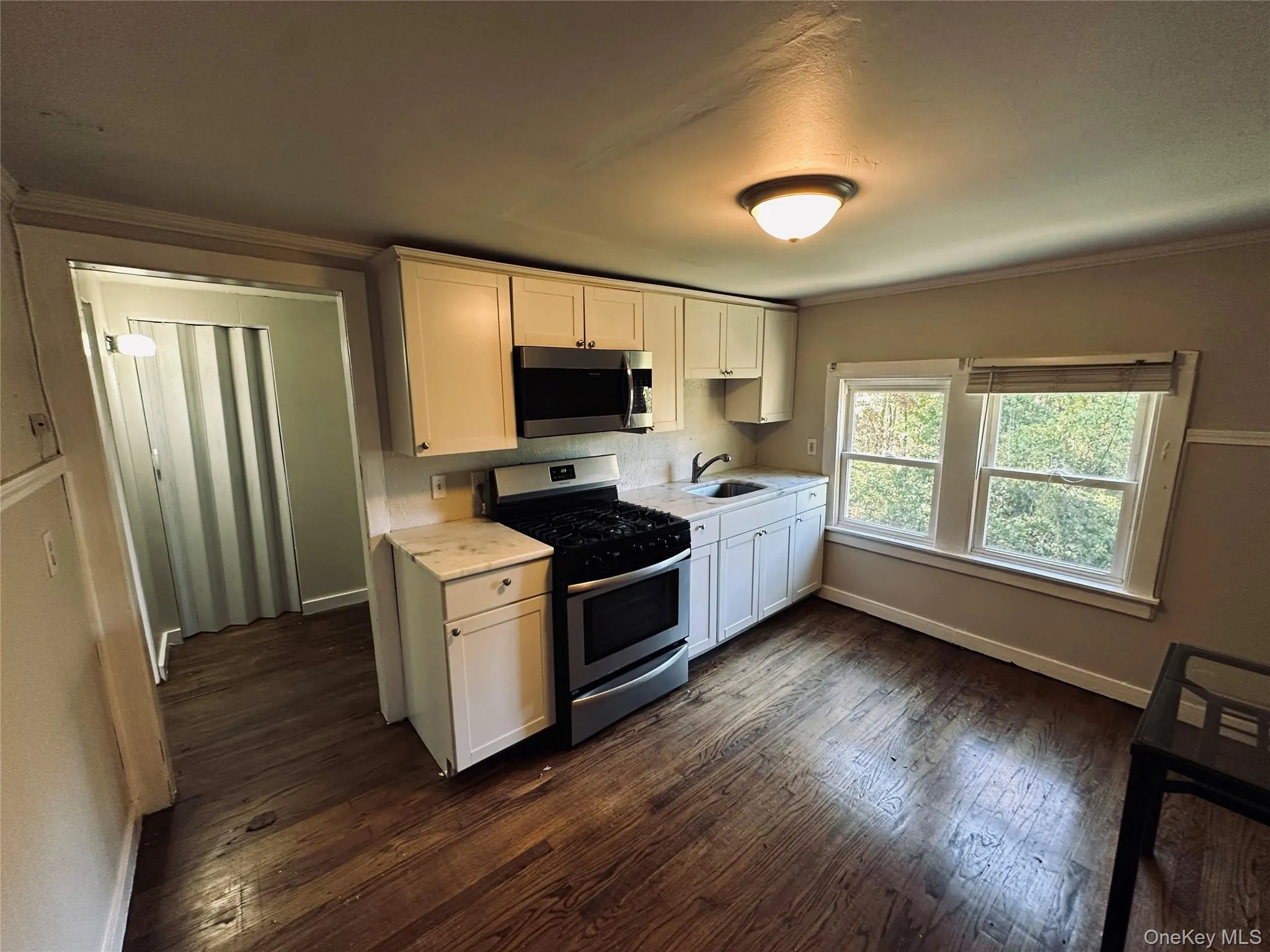 Kitchen featuring crown molding, light countertops, appliances with stainless steel finishes, white cabinetry, and dark wood finished floors Kitchen featuring crown molding, light countertops, appliances with stainless steel finishes, white cabinetry, and dark wood finished floors