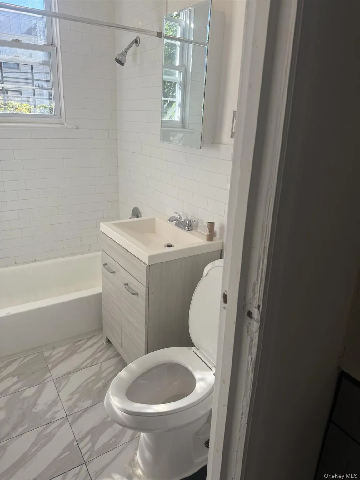 Bathroom with vanity, shower / bath combination, healthy amount of natural light, light marble finish floors, and tile walls Bathroom with vanity, shower / bath combination, healthy amount of natural light, light marble finish floors, and tile walls