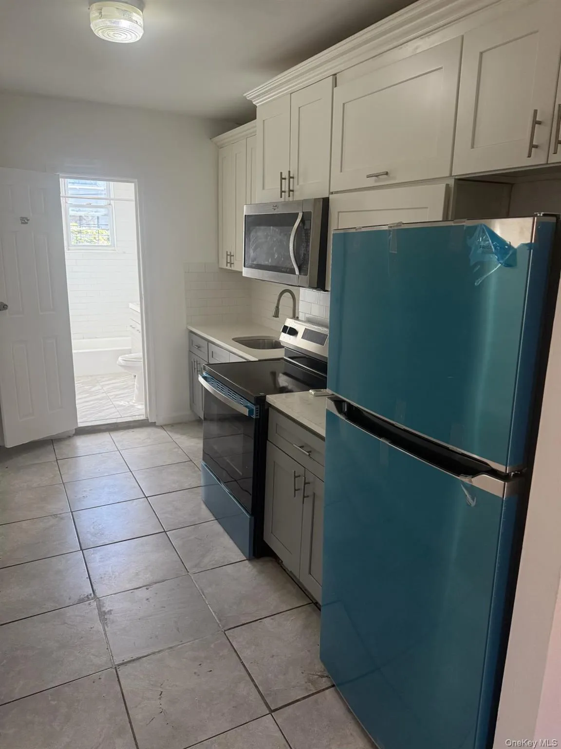 Kitchen featuring stainless steel appliances, light tile patterned flooring, decorative backsplash, light stone countertops, and gray cabinetry Kitchen featuring stainless steel appliances, light tile patterned flooring, decorative backsplash, light stone countertops, and gray cabinetry