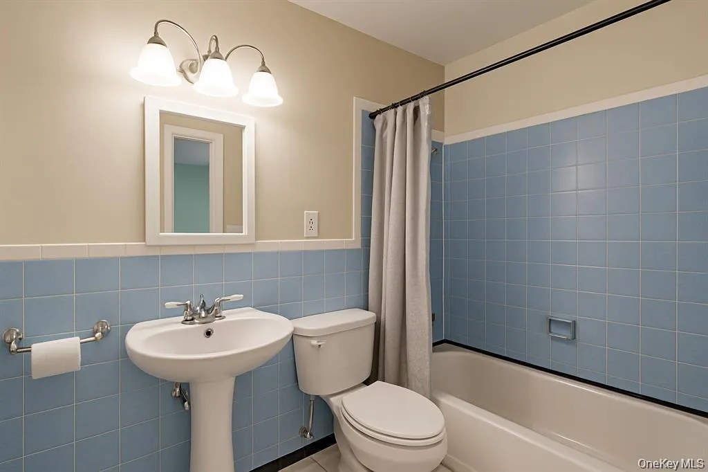 Bathroom with shower / bathtub combination with curtain, tile walls, and wainscoting Bathroom with shower / bathtub combination with curtain, tile walls, and wainscoting