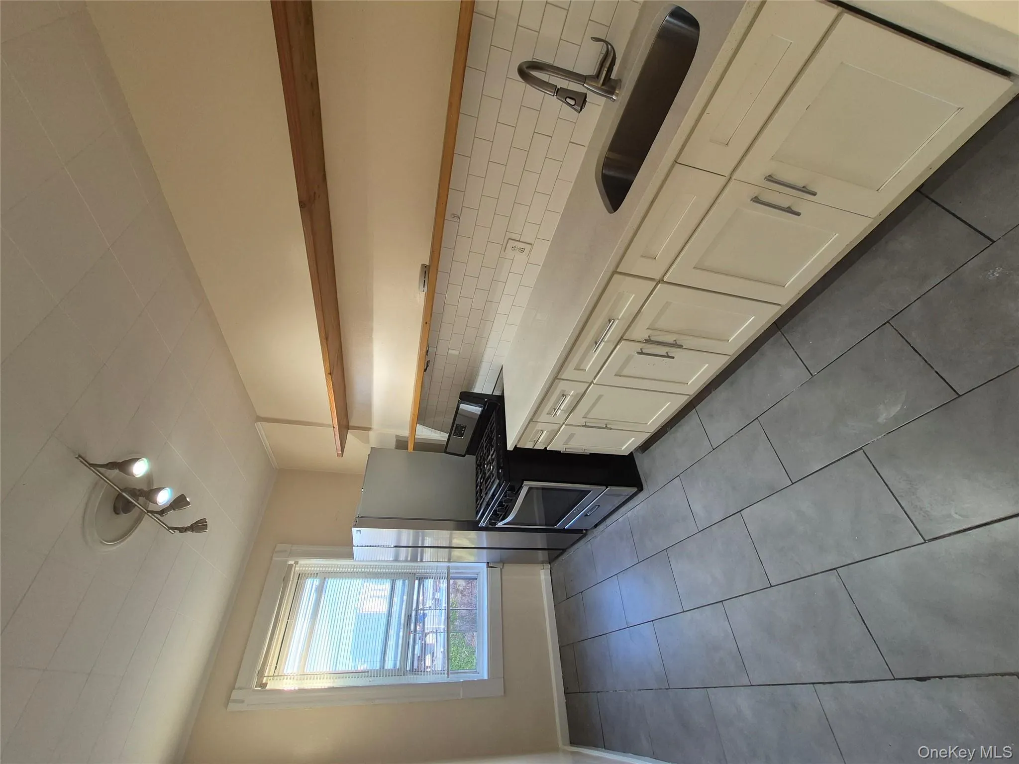 Kitchen with dark tile patterned flooring, open shelves, stainless steel stove, backsplash, and track lighting Kitchen with dark tile patterned flooring, open shelves, stainless steel stove, backsplash, and track lighting
