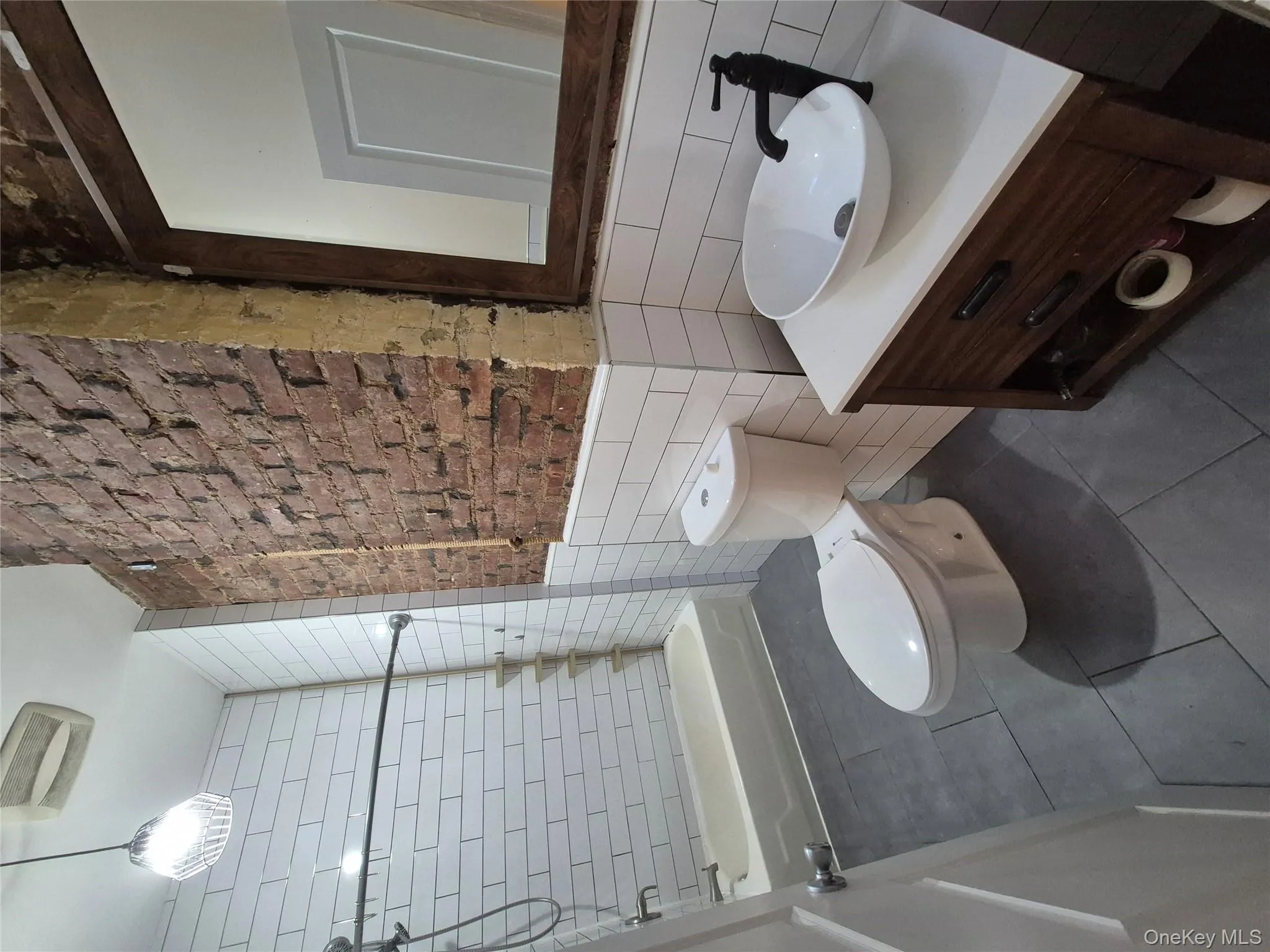 Bathroom featuring shower / tub combination, tile walls, vanity, dark tile patterned flooring, and a wainscoted wall Bathroom featuring shower / tub combination, tile walls, vanity, dark tile patterned flooring, and a wainscoted wall
