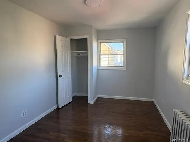 Large bedroom with radiator heating unit, dark wood-style floors, and a closet Large bedroom with radiator heating unit, dark wood-style floors, and a closet