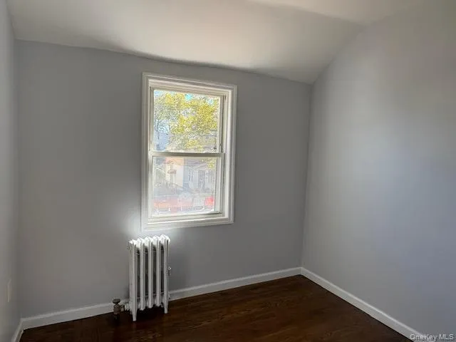 Bedroom with radiator, dark wood-style flooring, and lofted ceiling Bedroom with radiator, dark wood-style flooring, and lofted ceiling