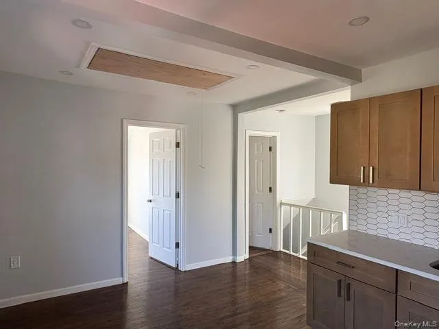 Kitchen featuring tasteful backsplash, light stone counters, dark wood finished floors, and brown cabinetry Kitchen featuring tasteful backsplash, light stone counters, dark wood finished floors, and brown cabinetry