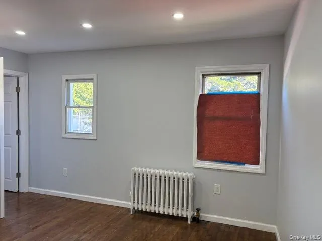 Empty room with radiator heating unit, dark wood-style floors, and recessed lighting Empty room with radiator heating unit, dark wood-style floors, and recessed lighting