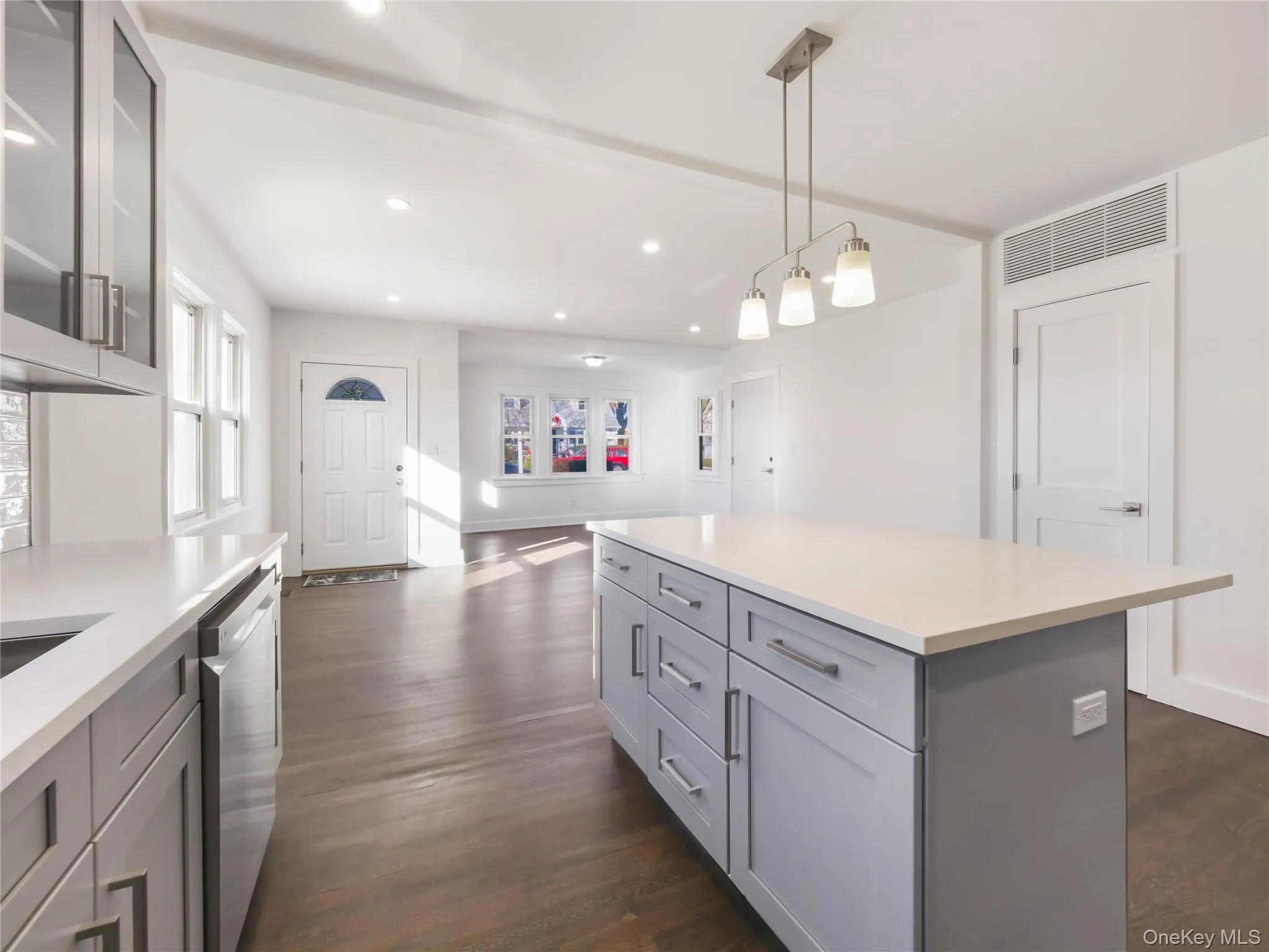 Kitchen with a kitchen island, decorative light fixtures, gray cabinetry, stainless steel dishwasher, and dark wood-type flooring Kitchen with a kitchen island, decorative light fixtures, gray cabinetry, stainless steel dishwasher, and dark wood-type flooring