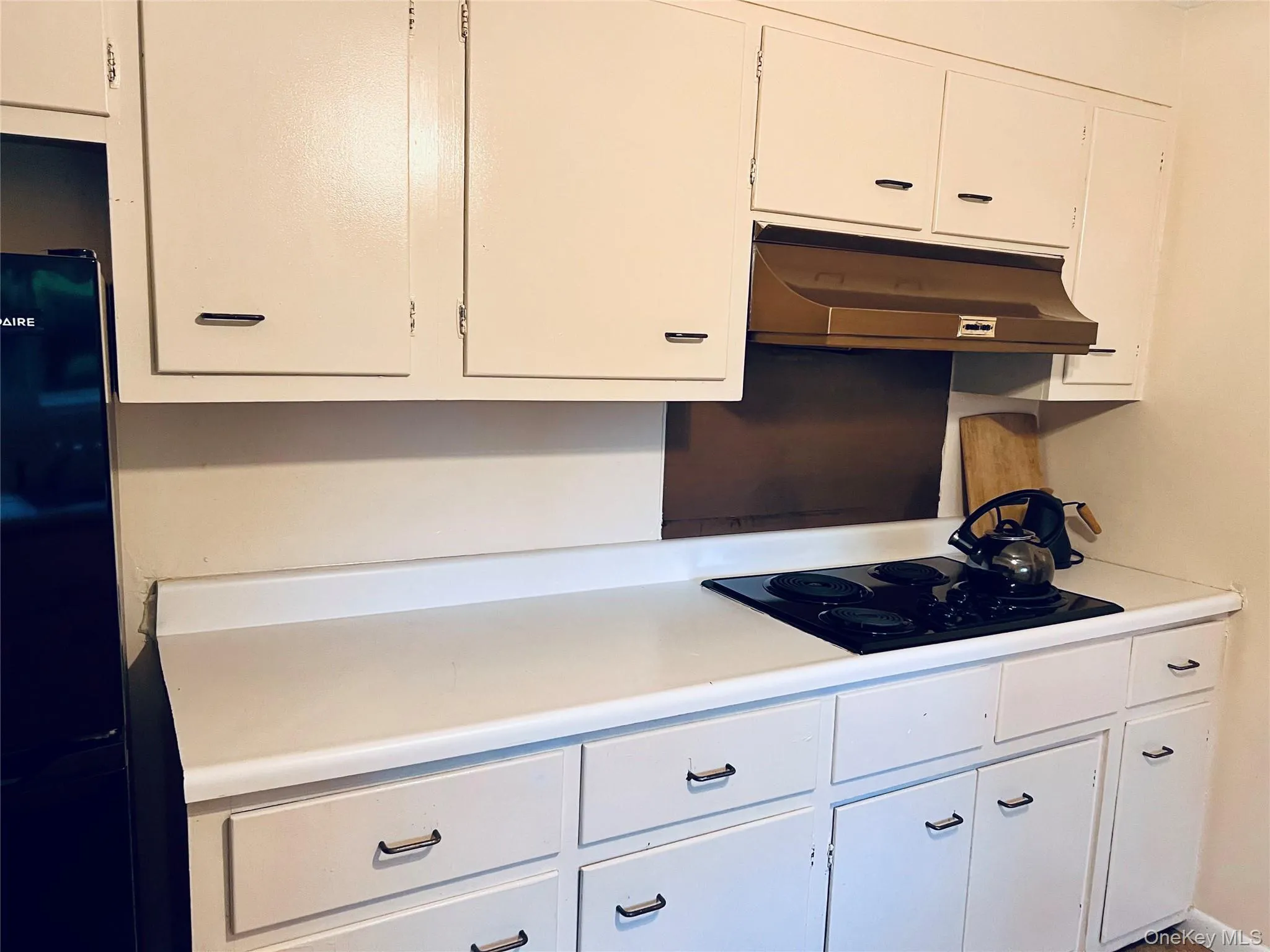 Kitchen with white cabinets, light countertops, under cabinet range hood, and black appliances Kitchen with white cabinets, light countertops, under cabinet range hood, and black appliances