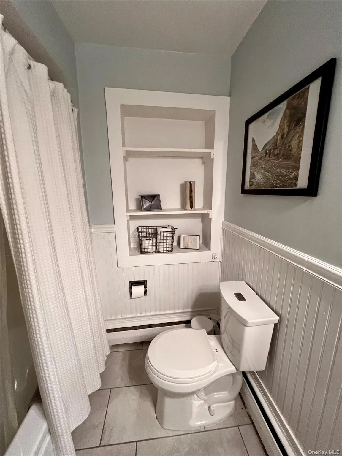 Full bath with a baseboard heating unit, light tile patterned floors, and shower / bathtub combination with curtain Full bath with a baseboard heating unit, light tile patterned floors, and shower / bathtub combination with curtain