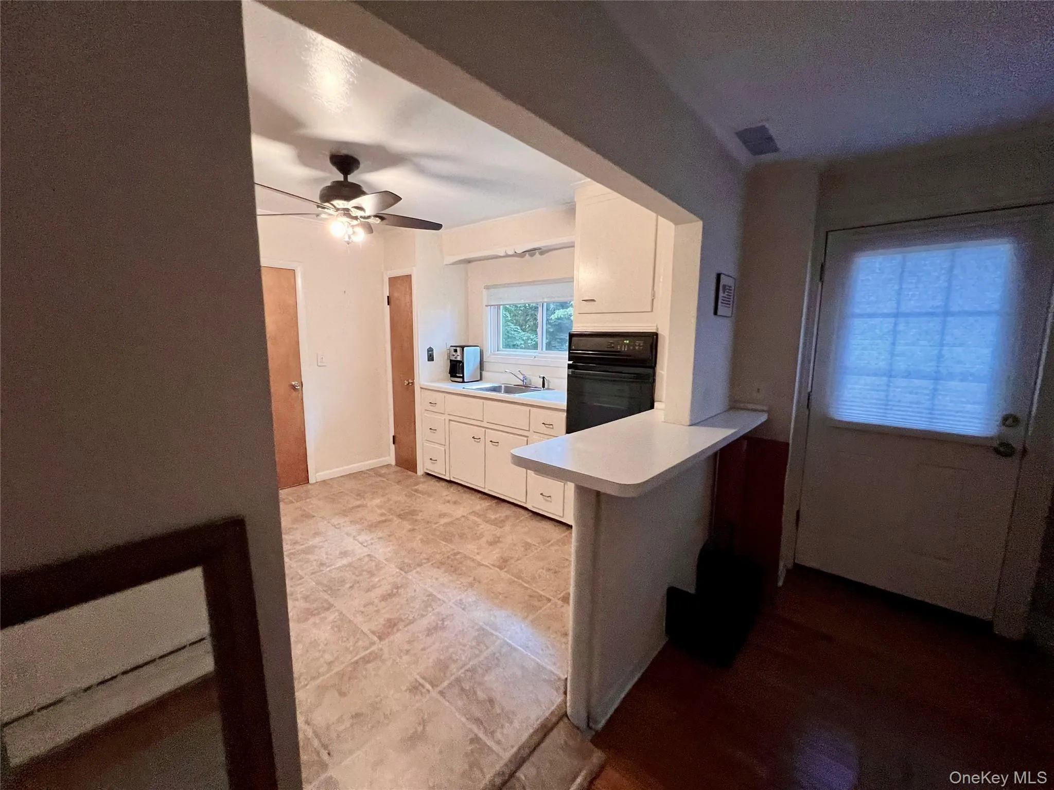 Kitchen featuring light countertops, black oven, white cabinetry, a peninsula, and ceiling fan Kitchen featuring light countertops, black oven, white cabinetry, a peninsula, and ceiling fan