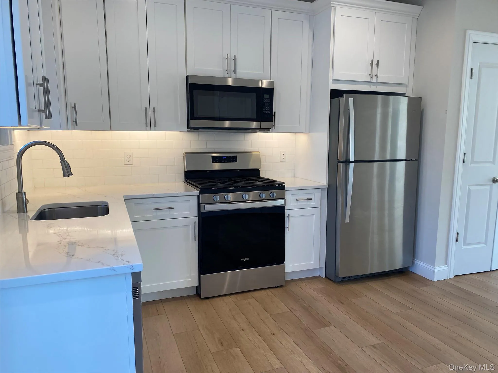 Kitchen featuring appliances with stainless steel finishes, white cabinets, light wood-style floors, light stone countertops, and tasteful backsplash Kitchen featuring appliances with stainless steel finishes, white cabinets, light wood-style floors, light stone countertops, and tasteful backsplash