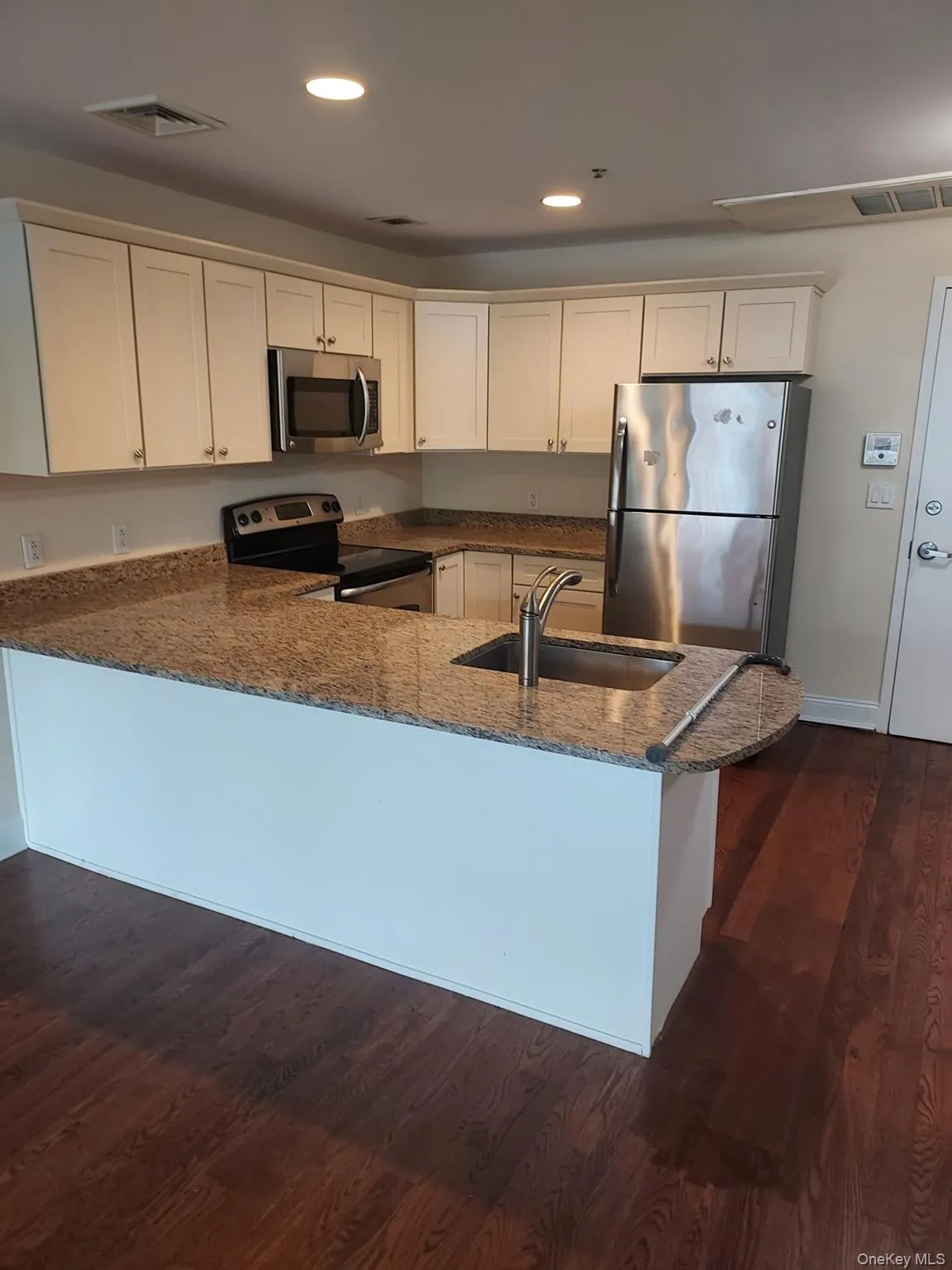 Kitchen featuring dark stone countertops, stainless steel appliances, a peninsula, dark wood finished floors, and recessed lighting Kitchen featuring dark stone countertops, stainless steel appliances, a peninsula, dark wood finished floors, and recessed lighting