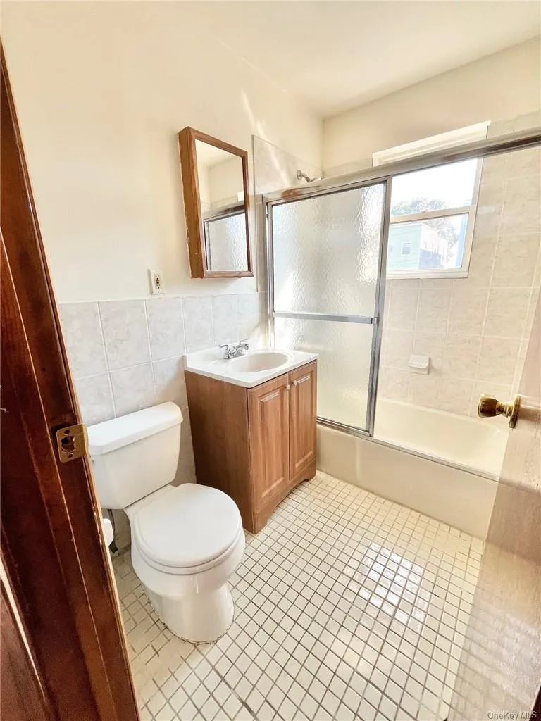 Full bathroom with enclosed tub / shower combo, tile walls, toilet, vanity, and tile patterned floors Full bathroom with enclosed tub / shower combo, tile walls, toilet, vanity, and tile patterned floors