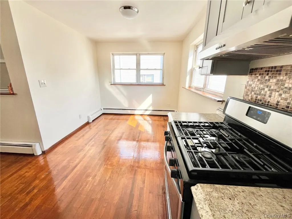 Kitchen with baseboard heating, stainless steel gas range oven, light hardwood / wood-style flooring, and backsplash Kitchen with baseboard heating, stainless steel gas range oven, light hardwood / wood-style flooring, and backsplash