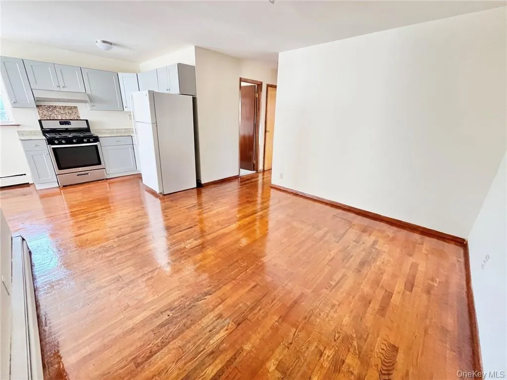 Kitchen featuring gray cabinetry, baseboard heating, stainless steel range, light hardwood / wood-style flooring, and white refrigerator Kitchen featuring gray cabinetry, baseboard heating, stainless steel range, light hardwood / wood-style flooring, and white refrigerator