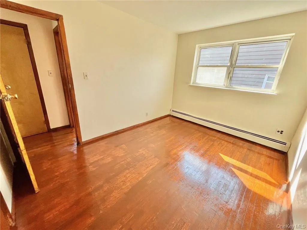 Empty room featuring baseboard heating and hardwood / wood-style floors Empty room featuring baseboard heating and hardwood / wood-style floors