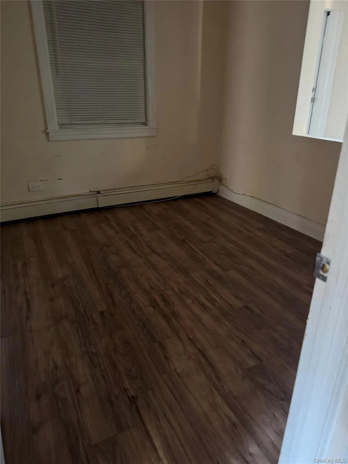Empty room featuring dark wood-style floors and a baseboard heating unit Empty room featuring dark wood-style floors and a baseboard heating unit