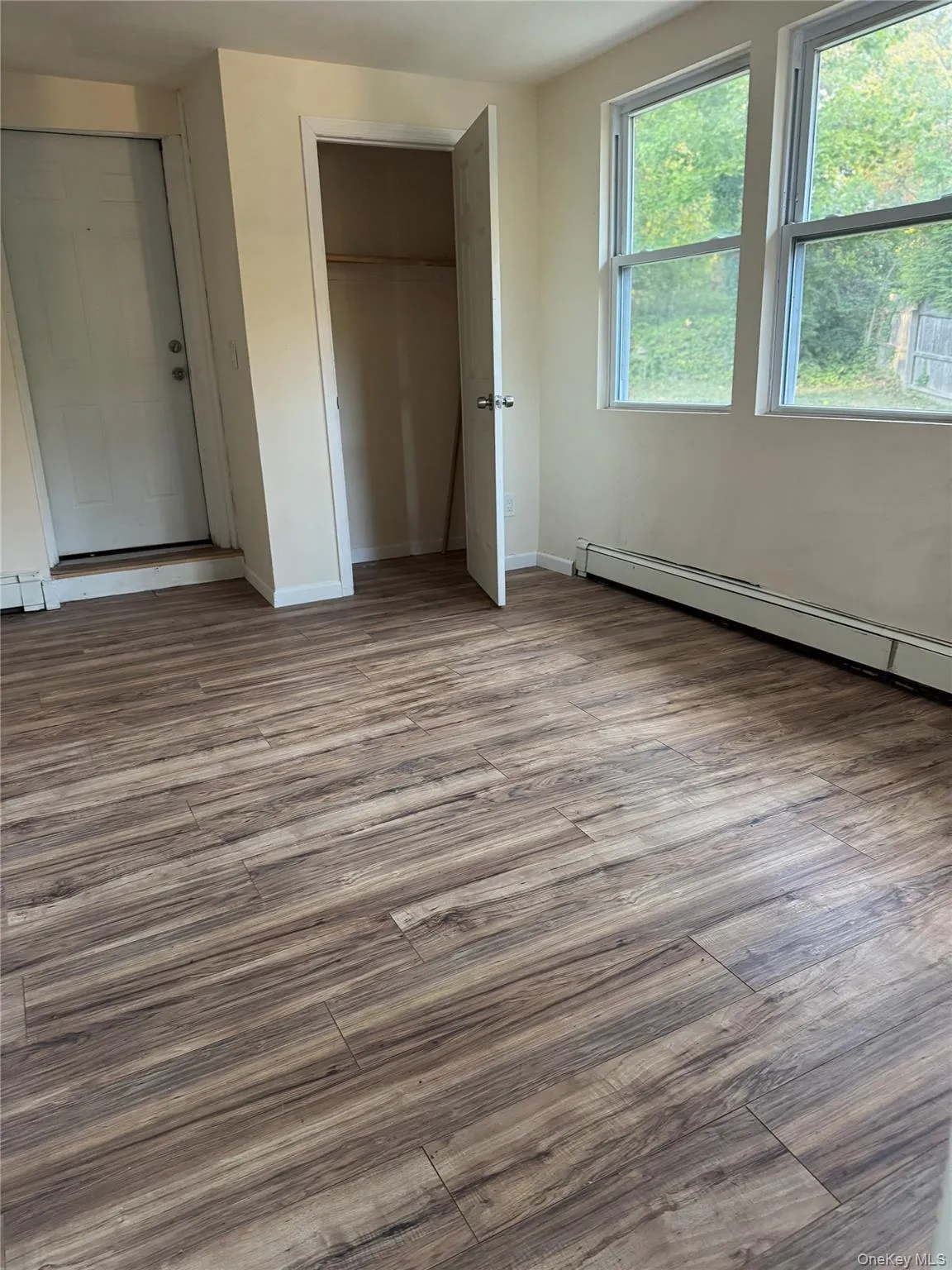 Unfurnished bedroom with baseboard heating, wood finished floors, and a closet Unfurnished bedroom with baseboard heating, wood finished floors, and a closet