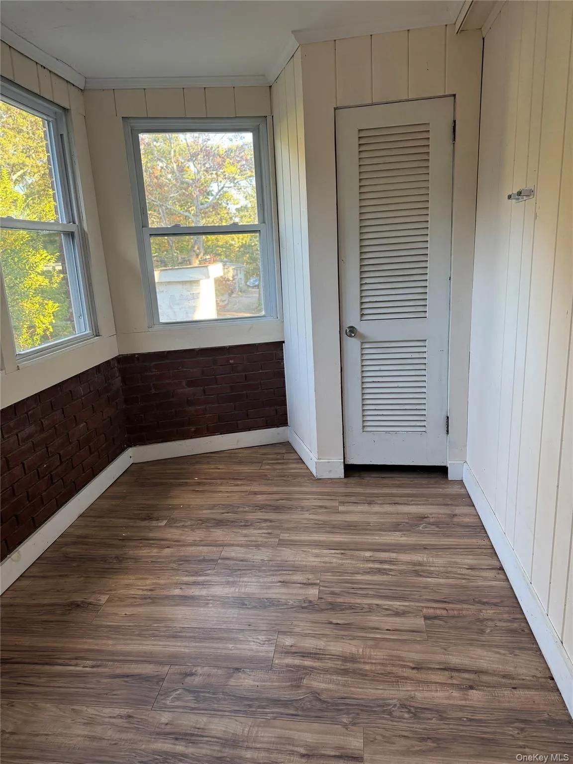 Unfurnished bedroom featuring crown molding, wood finished floors, a closet, and brick wall Unfurnished bedroom featuring crown molding, wood finished floors, a closet, and brick wall