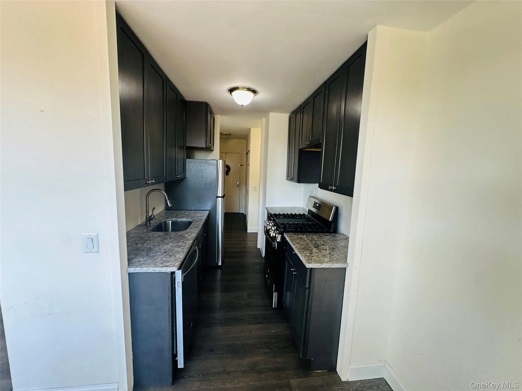 Kitchen featuring appliances with stainless steel finishes, dark wood-style flooring, dark cabinetry, and light countertops Kitchen featuring appliances with stainless steel finishes, dark wood-style flooring, dark cabinetry, and light countertops