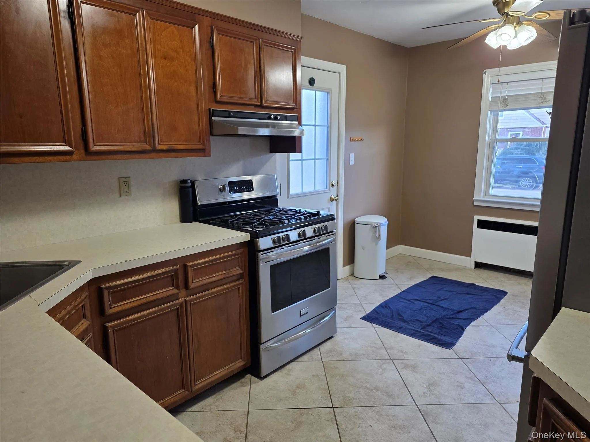 Kitchen featuring gas range, light countertops, radiator, a ceiling fan, and light tile patterned flooring Kitchen featuring gas range, light countertops, radiator, a ceiling fan, and light tile patterned flooring