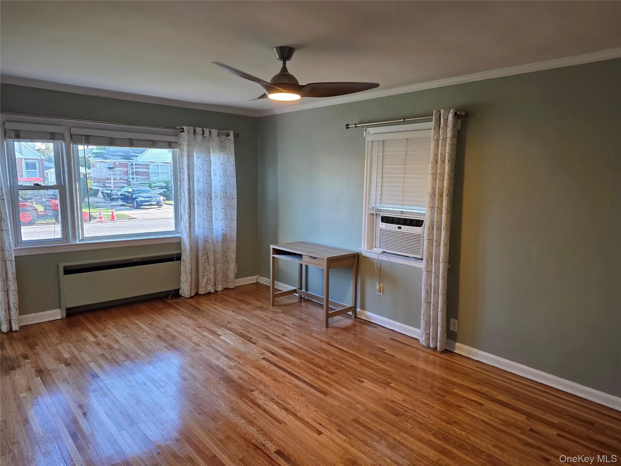 Huge living room featuring ornamental molding, light wood-style floors, a ceiling fan, radiator, and cooling unit Huge living room featuring ornamental molding, light wood-style floors, a ceiling fan, radiator, and cooling unit