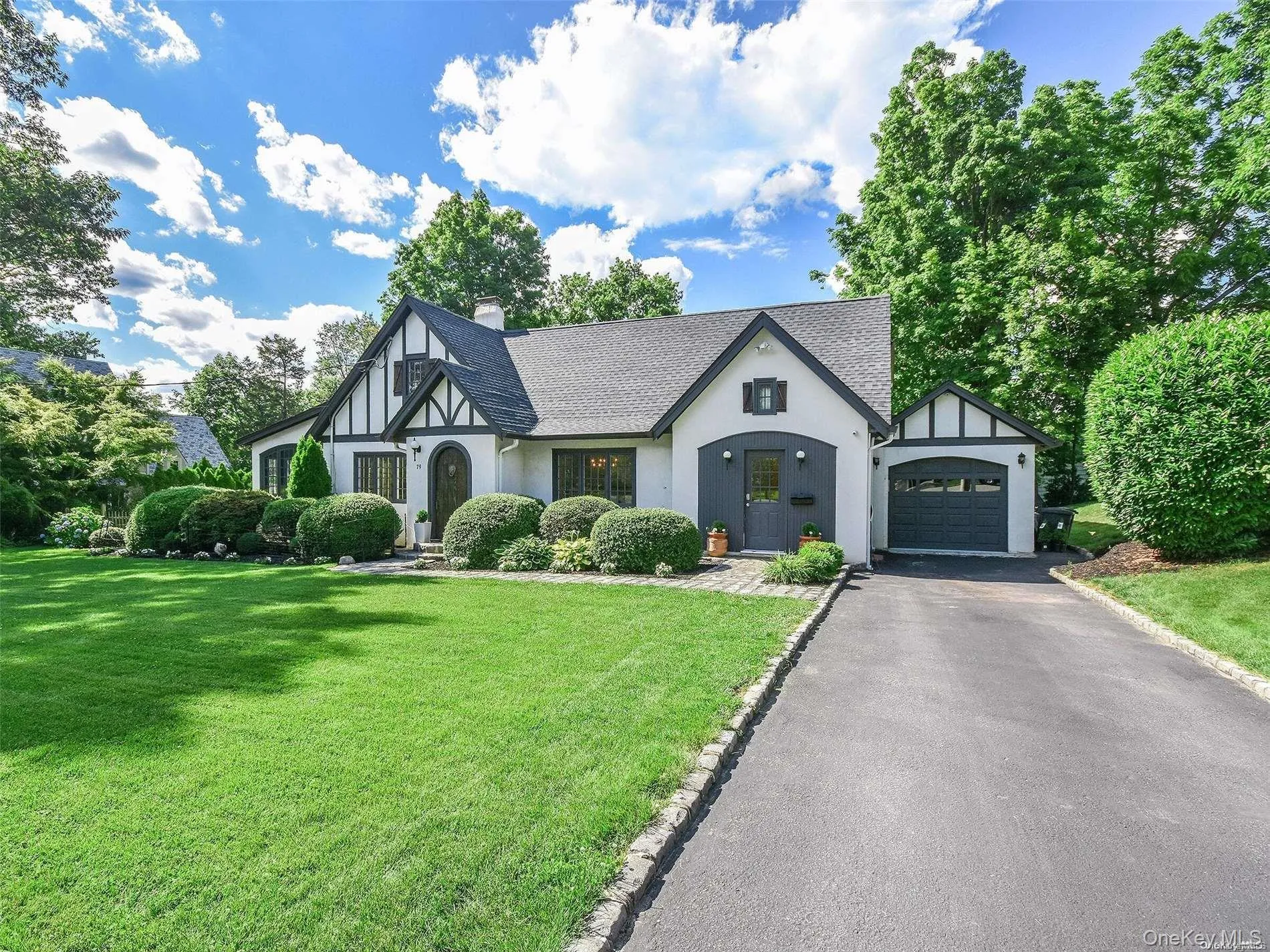 Tudor home with a garage, a front lawn, a chimney, asphalt driveway, and stucco siding Tudor home with a garage, a front lawn, a chimney, asphalt driveway, and stucco siding