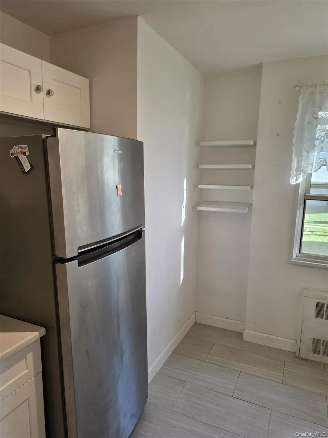 Kitchen featuring freestanding refrigerator, white cabinets, radiator heating unit, and wood finish floors Kitchen featuring freestanding refrigerator, white cabinets, radiator heating unit, and wood finish floors